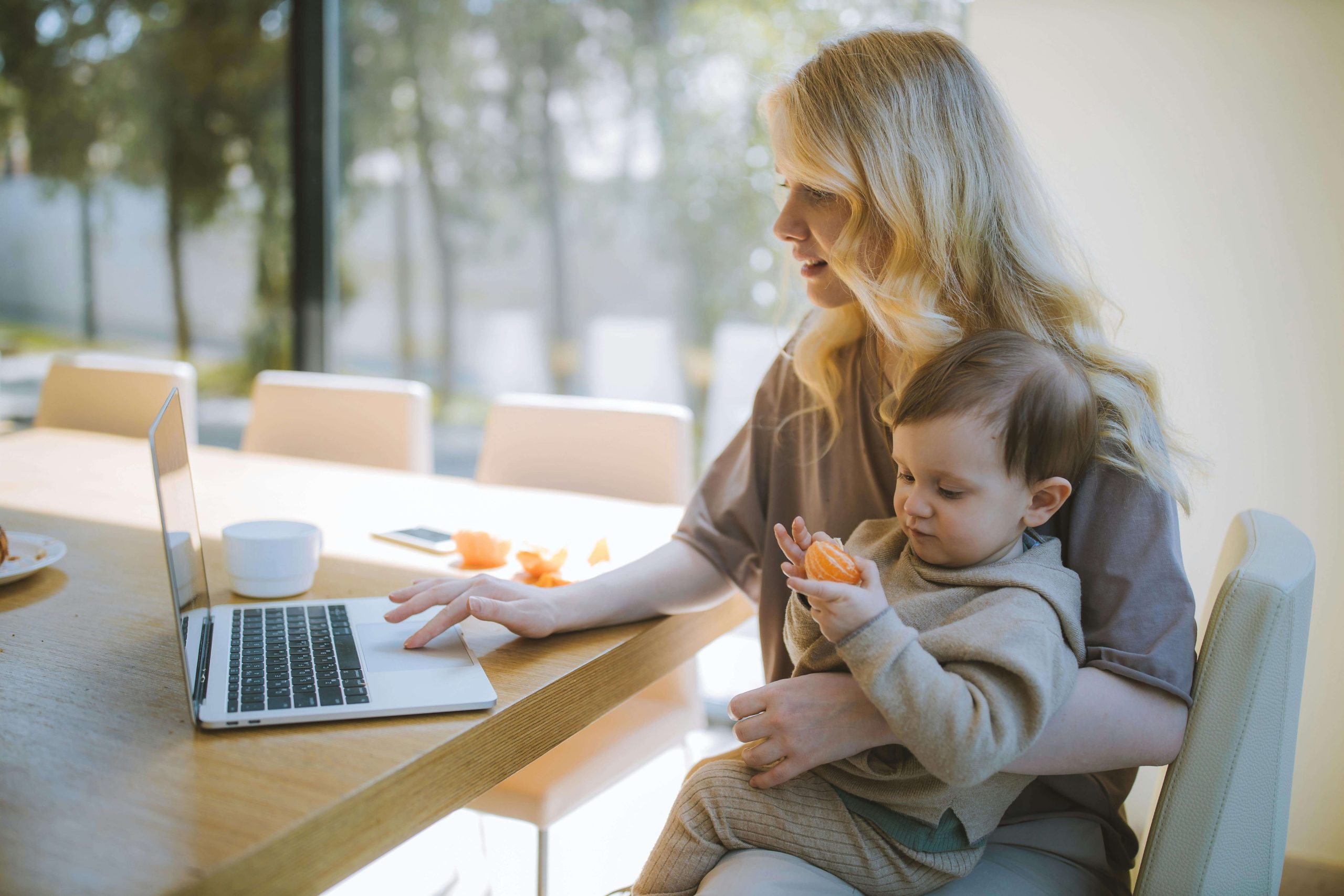 majka radi na laptopu s bebom u rukama